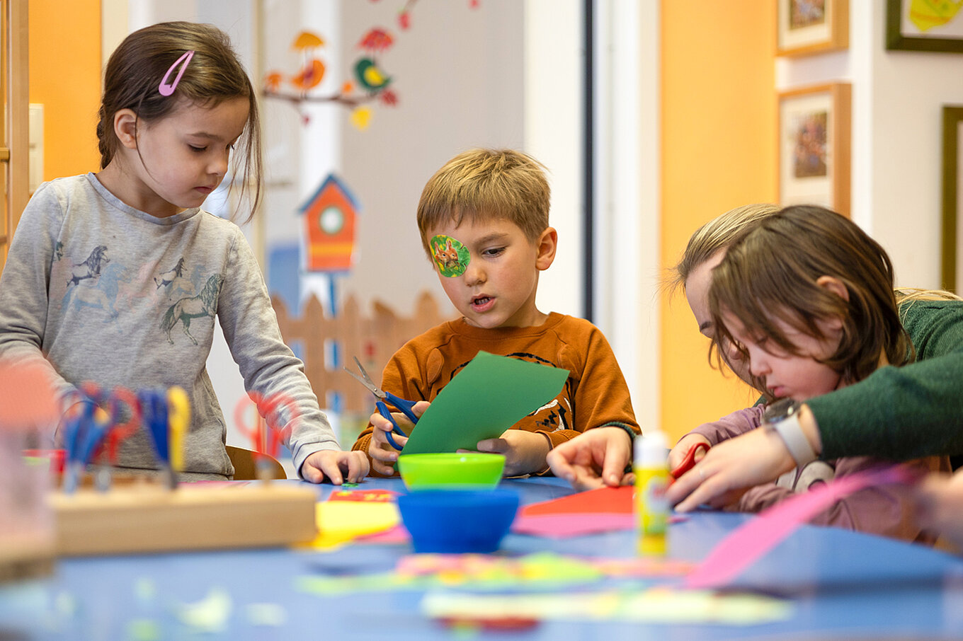 Erzieherin unterstützt Kinder beim Basteln mit Papier und Schere